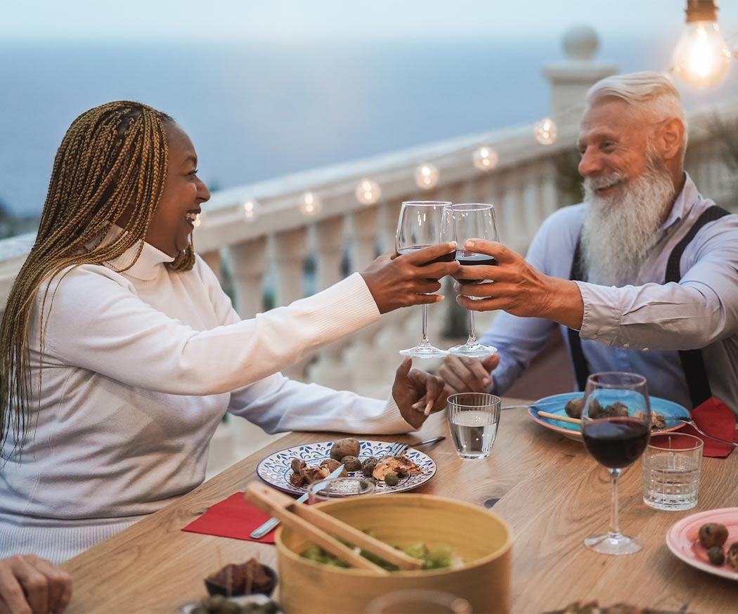 friends cheering wine glasses while eating at water front restaurant