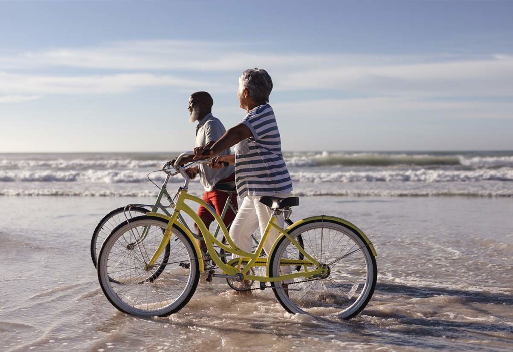 senior couple walking by their bikes on the beach retirement made simple schaumburg il